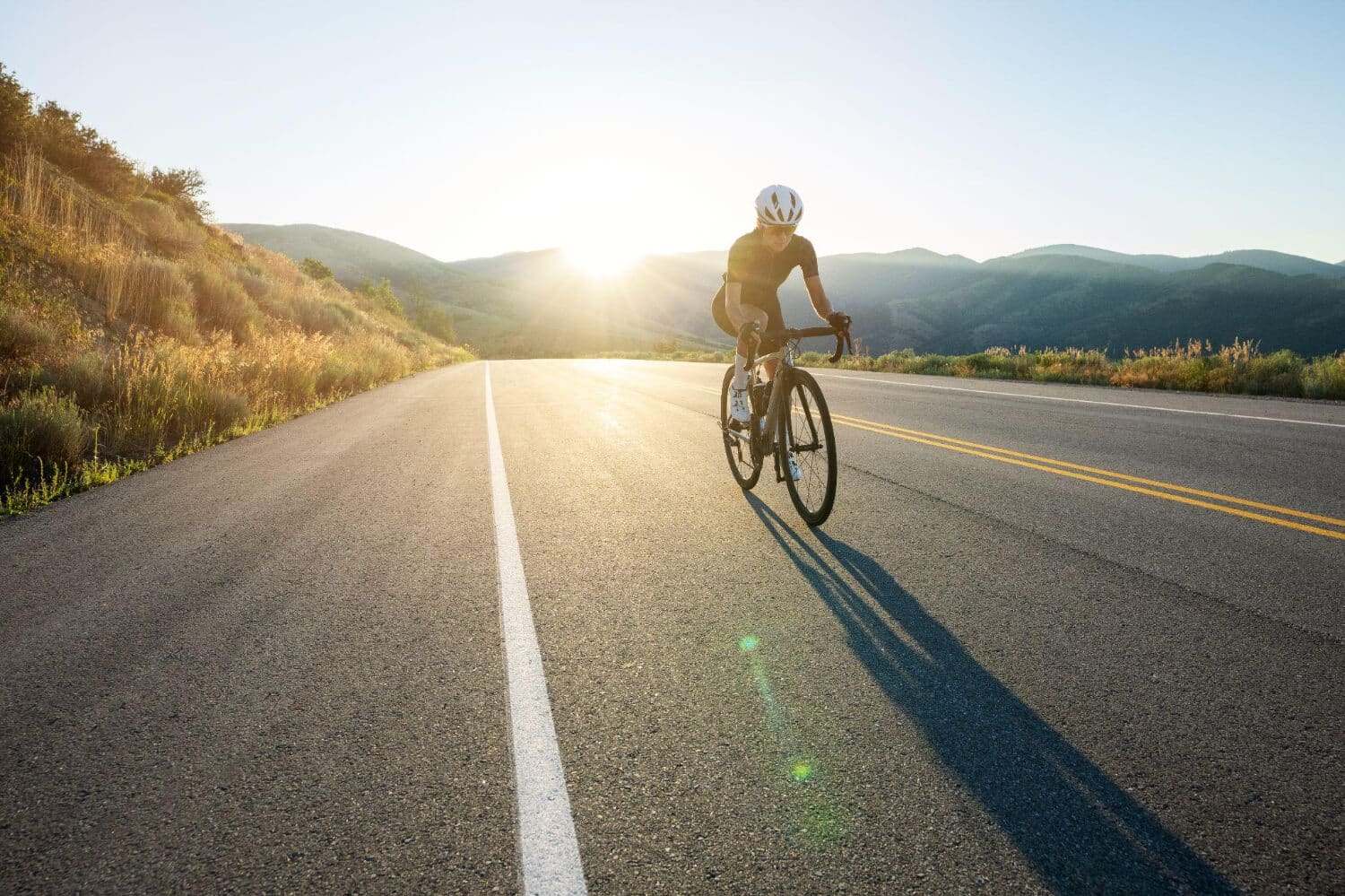 Cycliste en tenue noire sur un vélo de route en fibre de carbone TORAYCA®, roulant sur une route sinueuse en extérieur